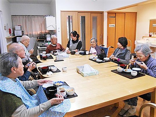 木製のテーブルを囲んで食事を楽しんでいる入居者。スタッフも一緒に座っている。