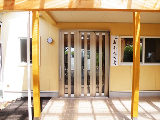 玄関には木製の屋根が付き、表札は手書きのような文字で書かれている。