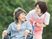 ピンクのエプロンを付けた若い女性スタッフと車いすの高齢女性が屋外で散歩をしている。