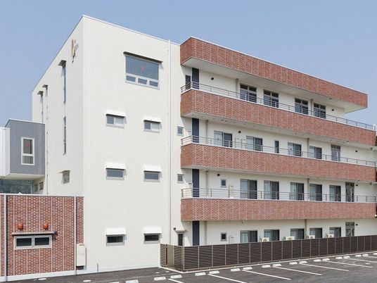 4階建ての建物は白を基調とした大きな建物で、各フロアにベランダがあり、駐車場もある。