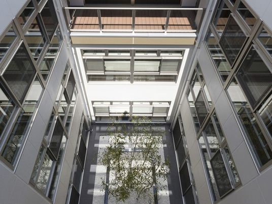 広々とした中庭が中央に設置され、たくさんの窓がある建物。上の階にはウッドデッキのテラスがある。
