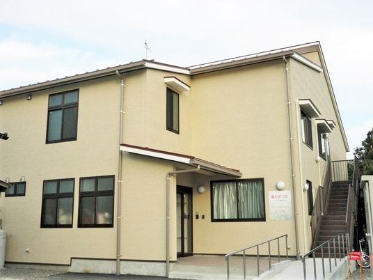 ベージュの２階建ての建物はバリアフリー設計。玄関には屋根が付いている。