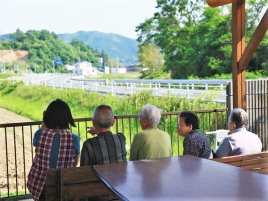 屋外のベンチに座って、周辺の自然を眺めている入居者とスタッフ。