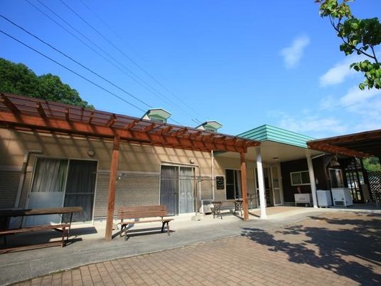 平屋建ての建物の前にはベンチやテーブルが置かれ、周辺には山がある。