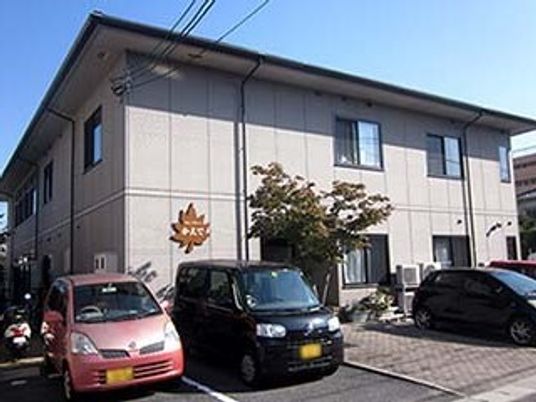 グレーを基調とした大きな2階建ての建物。ホームの前には駐車場がある。