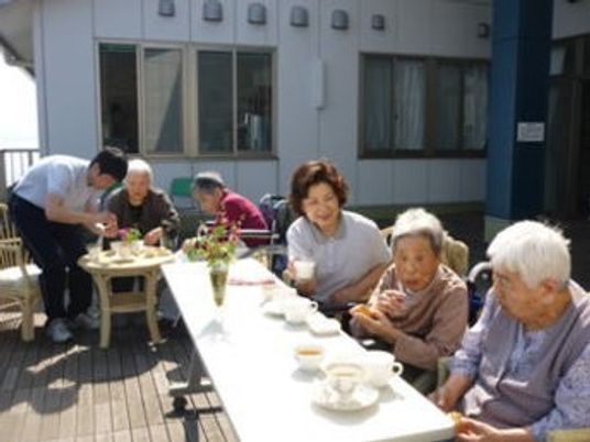 屋上のウッドデッキで食事を楽しんでいる様子。高齢者とスタッフの様子