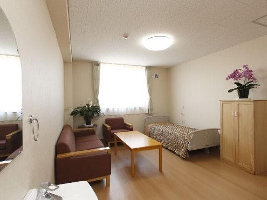 寝具付きのベッドやソファ、テーブル、収納家具などが置かれているフローリングの部屋には洗面所もある。