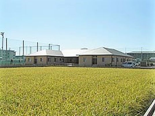 広々とした芝生のような広場とその向こう側にある建物。天気が良い日の外観写真
