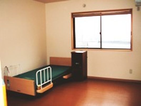 介護用ベッドや物置が置いてある小さなワンルームタイプの部屋。奥のほうに窓があり外につながっている