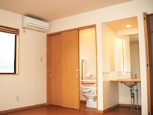 トイレと洗面台が付いている居室の設備の写真。手前にエアコンと窓がある