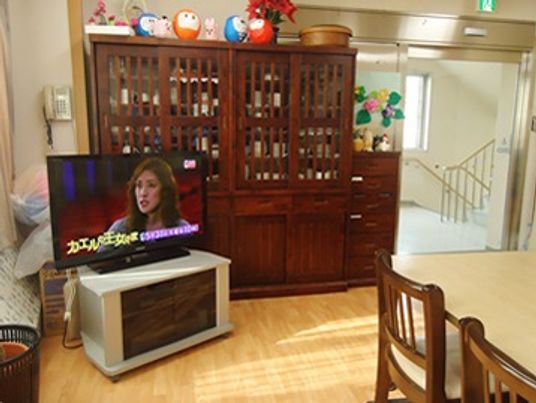タンス型の食器入れが置いてあるリビング。手前に椅子とテーブル、奥にテレビが置いてある様子
