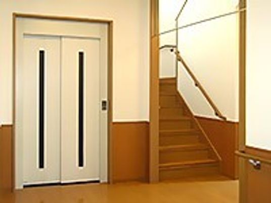 白いエレベーターと手すり付きの階段が隣同士に設置されている。