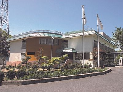 たくさんの木が植えられ、日当たりのいい場所に建っている2階建ての建物。旗も立っている。