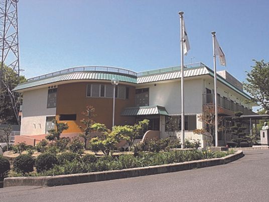 たくさんの木が植えられ、日当たりのいい場所に建っている2階建ての建物。旗も立っている。