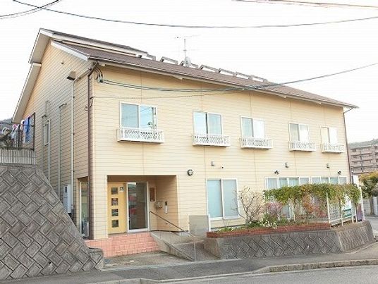 2階建ての建物は黄色っぽいベージュの外壁で敷地内には庭があり、草木が植えられている。周辺に高い建物はなく日当たりもよい。