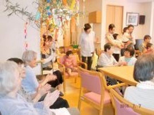 七夕飾りが飾られた共有スペースでイベントを楽しむ入居者と子連れの家族。