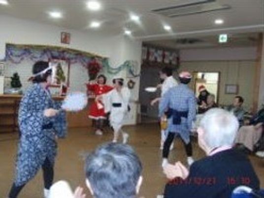 クリスマス会でボランティアによるひょっとこ踊りを見ている入居者の様子。