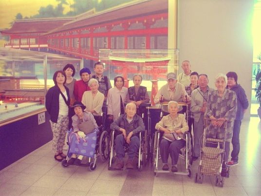 観光地での集合写真。車いすやシルバーカーを利用している入居者も同行している。