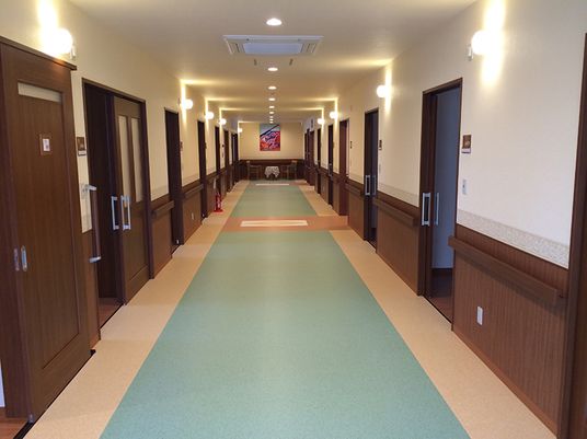 まっすぐな廊下の両サイドには手すりが設置され、居室のドアはスライド式。突き当りの壁には大きな絵画も飾られている。