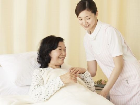 ベッドに寝ている女性に寄り添う看護師の写真。施設内の介護の様子