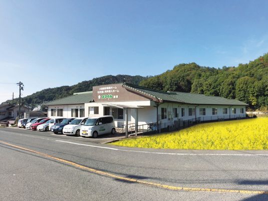 自然に囲まれた平屋建てのホームの周りには菜の花畑などがあり、広い駐車スペースもある。