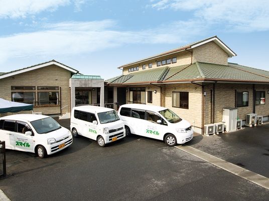 一般の住宅のような三角屋根が付いたホーム。ホームの駐車場にはホーム名が書かれた車が3台止まっている。