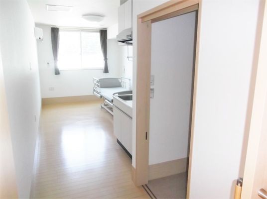 出入り口から居室を見渡した様子。ベッドやキッチン、トイレのドアが見える。