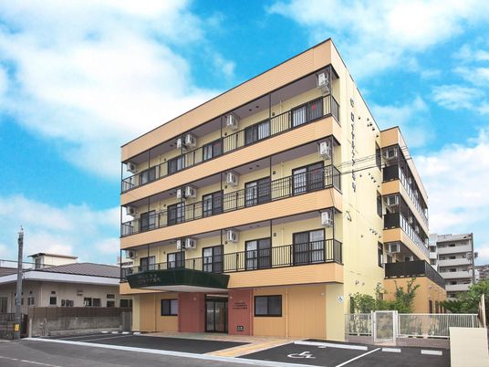 4階建ての建物の外壁はベージュ系で各フロアにベランダがあり、駐車場も完備されている。
