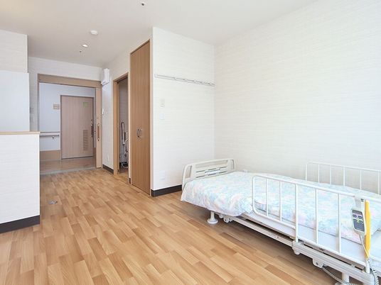 寝具付きのベッドが置かれ、クローゼットやトイレが付いたフローリングの部屋。