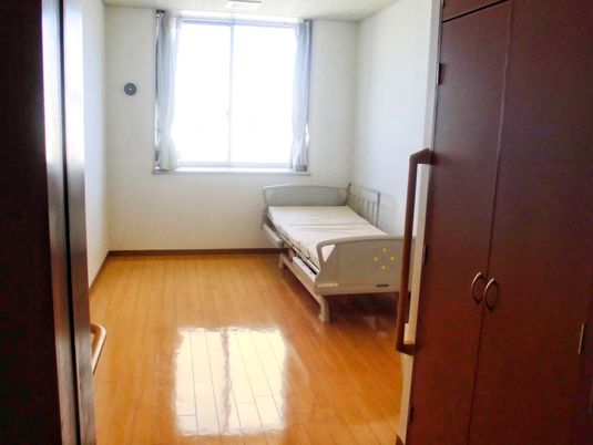 クローゼットや介護ベッドが置かれたフローリングの部屋にはカーテンが付いた大きな窓がある。