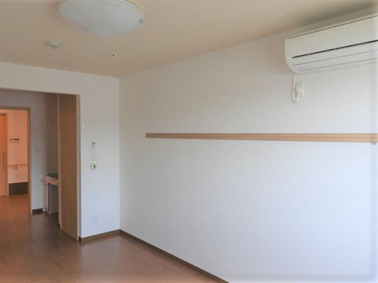 エアコンや照明、ピクチャーレールが設置されたフローリングの部屋には呼び出しボタンが付き、ドアの外には廊下がある。