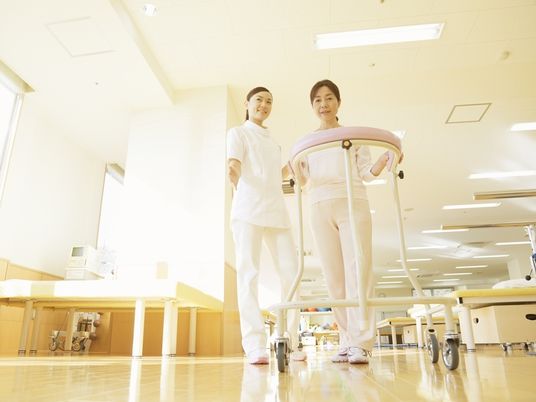 リハビリ器具を利用してリハビリに励んでいる高齢者と見守る看護師の写真