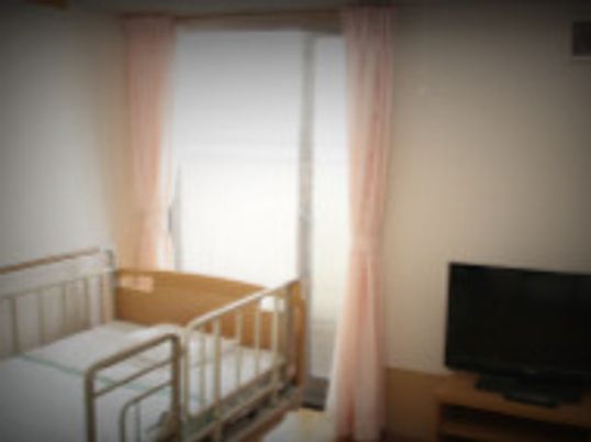 テレビや介護ベッドが置かれた居室にはレースカーテンとカーテンが付いた大きな窓がある。