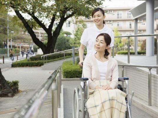 車いすに座っている女性とそれを押すスタッフの写真。外で移動している様子