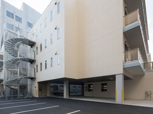 屋外階段やベランダが付いたベージュの建物は4階建ての建物。敷地内には駐車場がある。