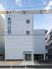 住宅名と併設事業所名が書かれている白い壁が印象的な4階建ての建物。玄関に続く白い道のそばには駐車場がある。