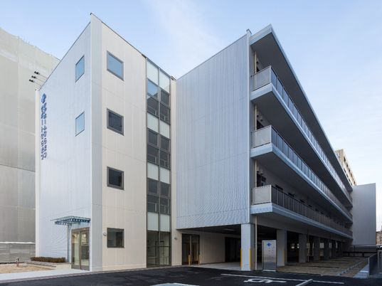 白を基調としている4階建ての建物。各フロアにベランダがあり、玄関には屋根があり、外壁には住宅名と併設事業所名が書かれている。