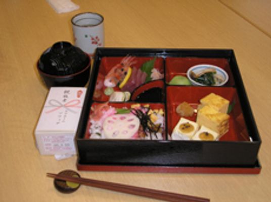 お重にきれいに詰められた食事例。重箱の外には吸い物や湯飲み、記念品が置かれている。