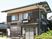 2階建ての木造建築には瓦の屋根が付き、一般の住宅のような外観。玄関先には椅子が2脚とベンチが置かれていて、周囲にも住宅がある。