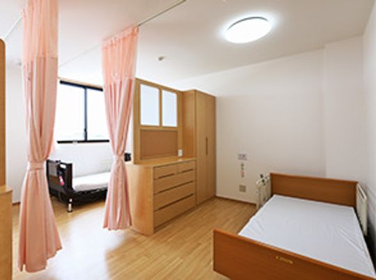 ４人部屋はピンクのカーテンで仕切られ、それぞれのスペースにベッドが置かれ、収納家具が設置されている。
