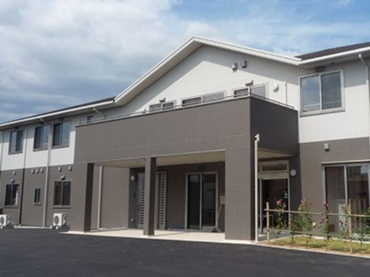 2階建ての建物。ブラウンと白のモダンなデザインで木も植えられている。