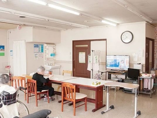 大きなブルーのソファが置かれているリビングの奥には靴が並べられたラックが置かれた玄関があり、家庭的な環境。