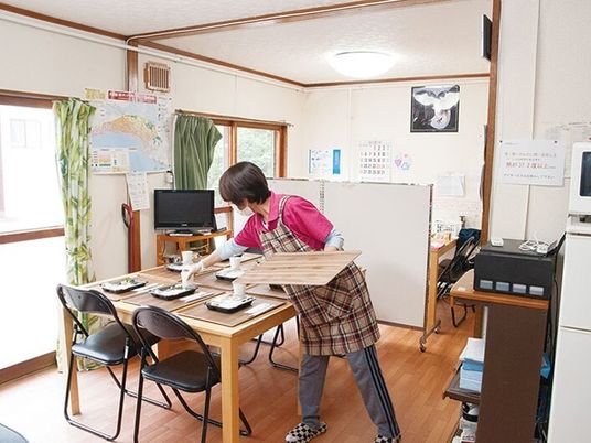 エプロンを付けた女性スタッフが食卓の準備をしているダイニングには大きな窓が付き明るい雰囲気。