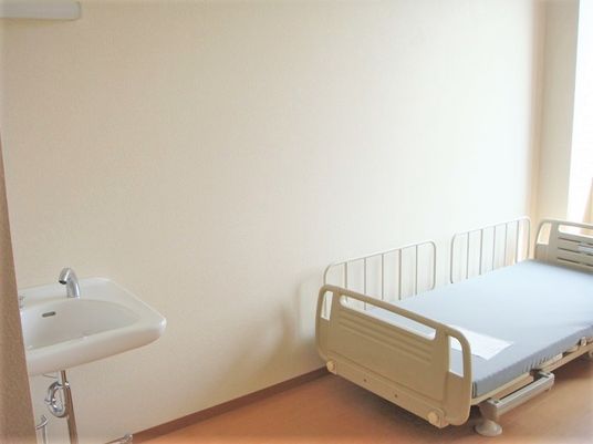 洗面台、ベッドが写っている居室の写真。奥のほうから日差しが差し込んでいる