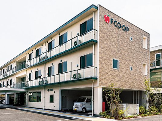 3階建ての建物は横に長く、レンガ調の外壁には住宅名が書かれ、シンボルマークのリンゴの絵もある。