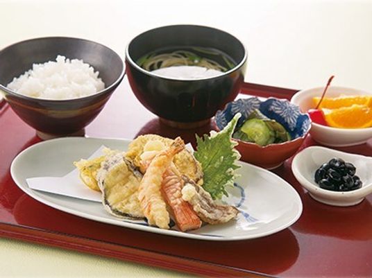 白いご飯に吸い物、天ぷらの盛り合わせや野菜の小鉢、フルーツなどが並べられた赤いトレー。