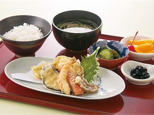 白いご飯に吸い物、天ぷらの盛り合わせや野菜の小鉢、フルーツなどが並べられた赤いトレー。