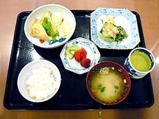 品数の多い食事。白いご飯に味噌汁、お茶、野菜たっぷりのおかずが並んでいる。