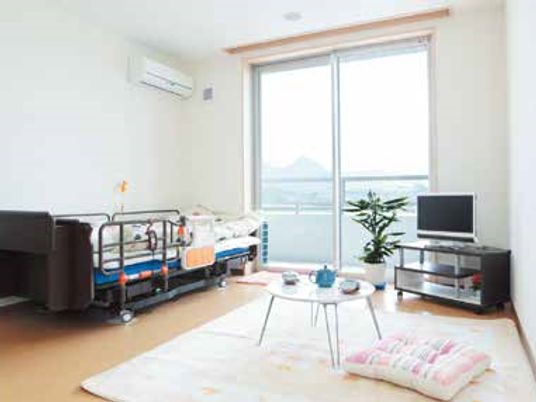 寝具付きのベッドやエアコン、テレビ、ローテーブルが置かれたフローリングの部屋には観葉植物がある。