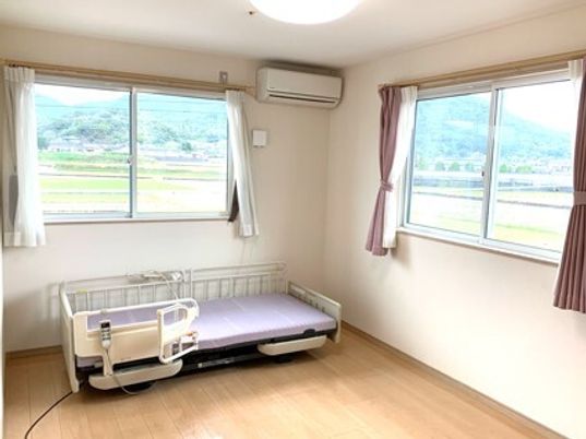 大きな窓が二つ付いたフローリングの部屋には介護ベッドやエアコンが設置され、窓の外には自然が広がっている。